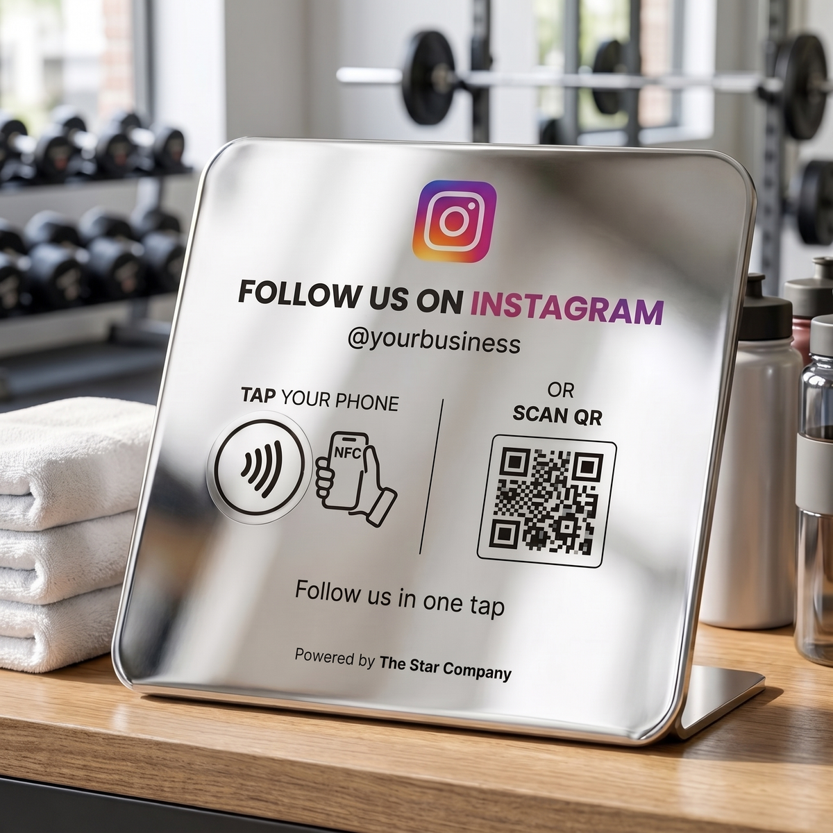 Steel Instagram Follow Plate on a gym reception desk beside towels and water bottles